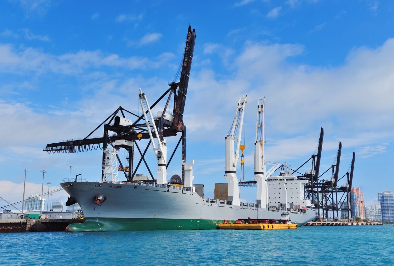 Cargo ship at Miami harbor with crane and blue sky over sea.